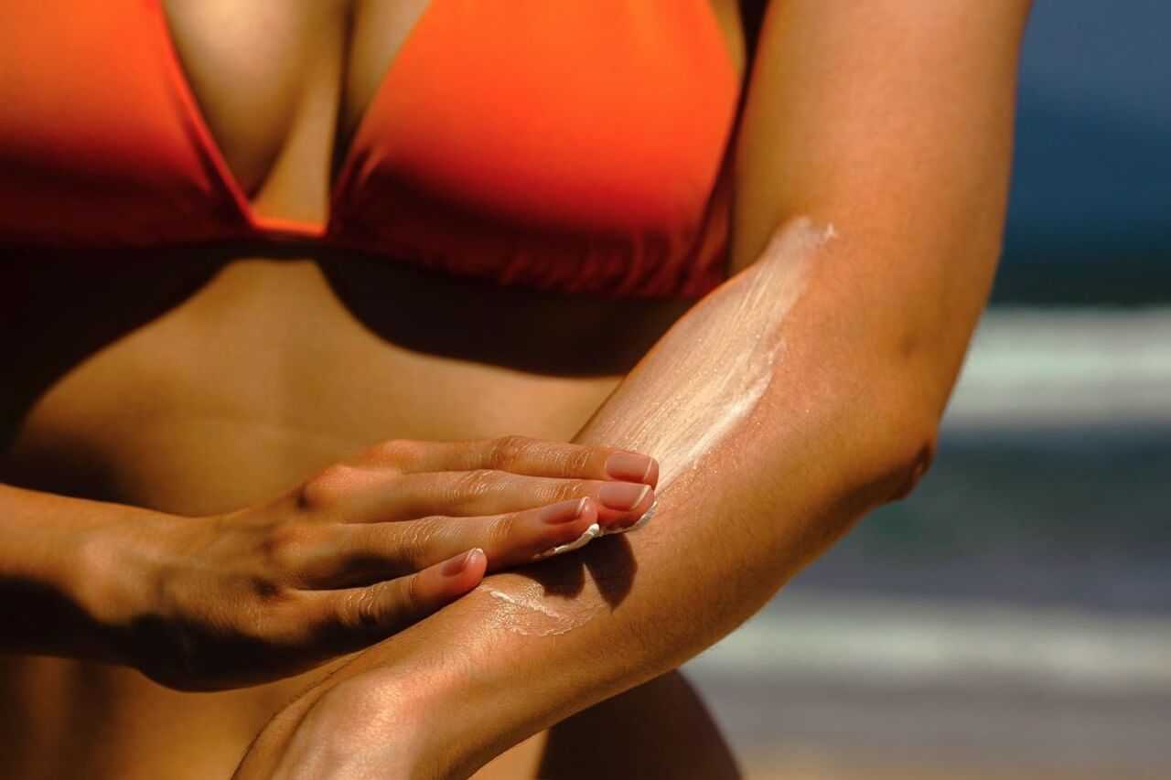 Applying sunscreen to arm on a sunny beach day.