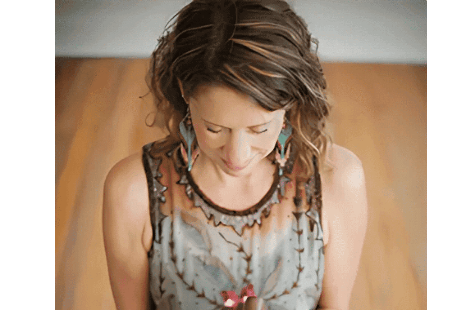 A woman in a patterned dress holding a small flower, looking downward.