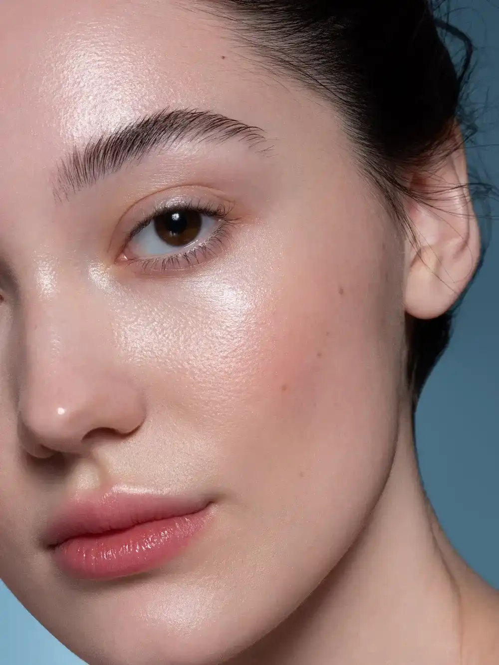 Close-up of a woman's face with clear skin and a neutral expression against a blue background.